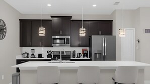 A modern kitchen with dark cabinets, a large island with bar stools, stainless steel appliances, and pendant lighting. - 4BR house at Storey Lake Resort 9min Disney (Kissimmee)