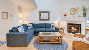 Un salon avec un canapé bleu, une table basse en verre, une cheminée et une petite table d’appoint avec une lampe.