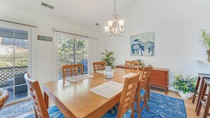 Un coin repas comprenant une table en bois, des chaises, un lustre, un tableau et une plante en pot.