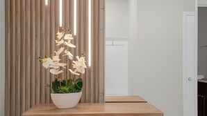 A room with a wooden table, a white vase with white flowers, and a vertical striped wall.