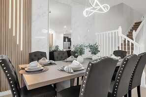 Een moderne eethoek met een marmeren wand, een trap en een kroonluchter.