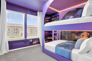 Een kamer met een stapelbed, grote ramen met zonwering en uitzicht op gebouwen.