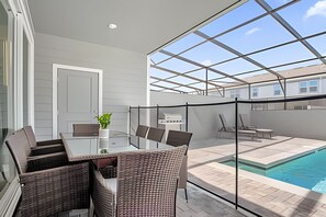Een overdekt terras met glazen dak, zitplaatsen buiten en een zwembad.