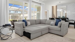 A modern living room with a sectional sofa, a dining area, and large windows offering a view of the outside.