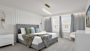 A modern bedroom with a large bed, bedside tables, a dresser, and a window with curtains.