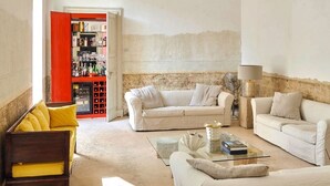 Un salon spacieux avec un plafond haut, un canapé blanc, un fauteuil jaune et une table basse en verre.