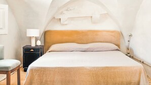 Une chambre à coucher avec un plafond voûté, un lit doté d’une tête de lit beige, une table de chevet avec une lampe et une chaise.