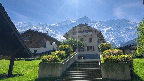 A building with a staircase leading to a door, surrounded by greenery and snow-capped mountains in the background. - Cozy mountain studio | Summer pool + parking (Les Houches)