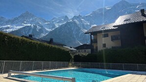A swimming pool with a mountain backdrop, a building with balconies, and a clear sky. - Cozy mountain studio | Summer pool + parking (Les Houches)