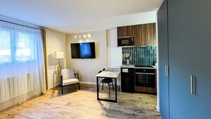 A modern kitchen with a flat-screen TV, wooden cabinets, and a built-in oven. - Cozy mountain studio | Summer pool + parking (Les Houches)