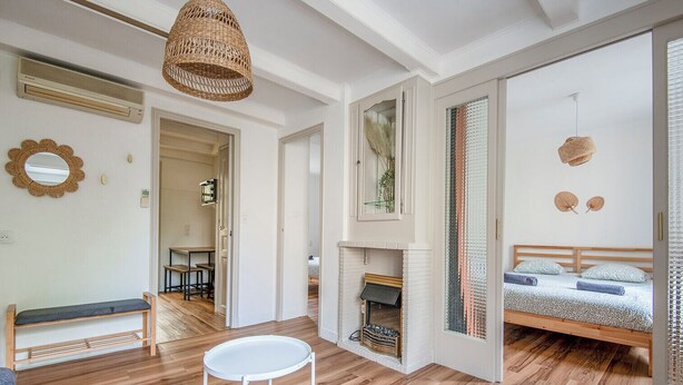 A modern bedroom with a bed, a small table, a bench, a fireplace, and a large window.