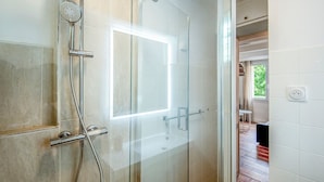 A modern bathroom with a glass shower enclosure, a visible light switch, and a door leading to another room.