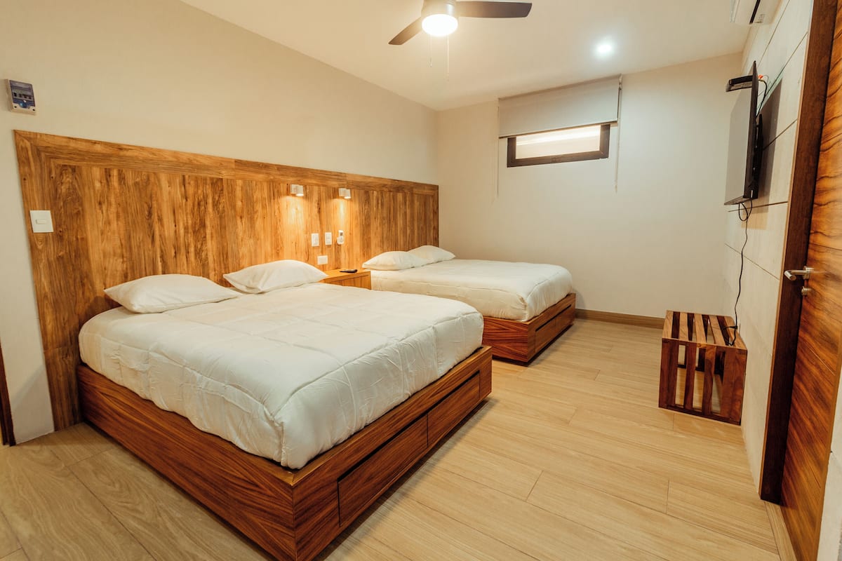 A hotel room with two wooden beds, a ceiling fan, and a TV mounted on the wall.