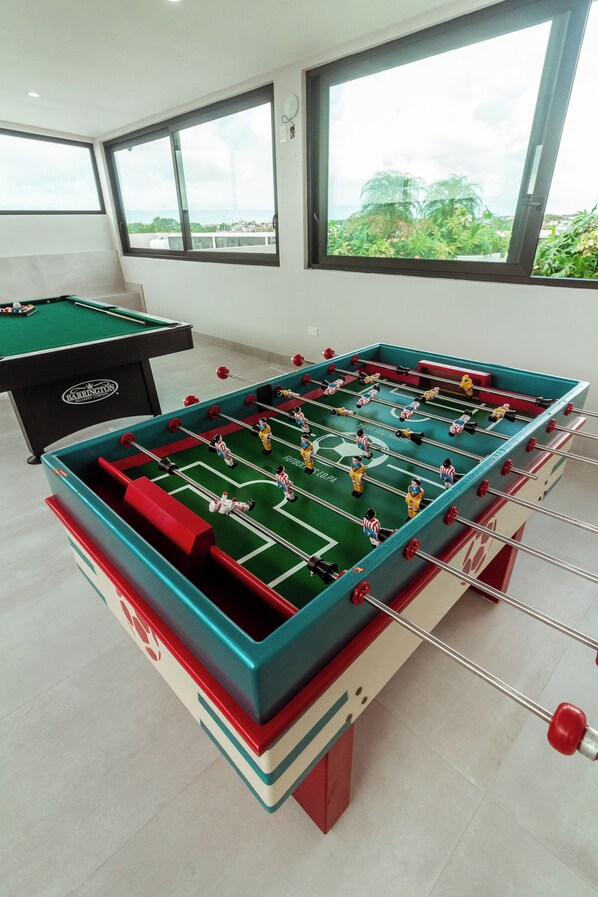 Une table de baby-foot dans une pièce dotée de grandes fenêtres et d’une table de billard.
