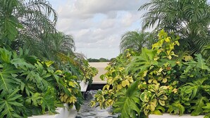 A narrow water channel flanked by lush greenery and white planters, leading to a distant structure. - Xoza Hotel Urban Escape (Cancun)
