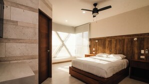 A modern bedroom with a wooden headboard, a large bed, a nightstand, and a ceiling fan. - Xoza Hotel Urban Escape (Cancun)
