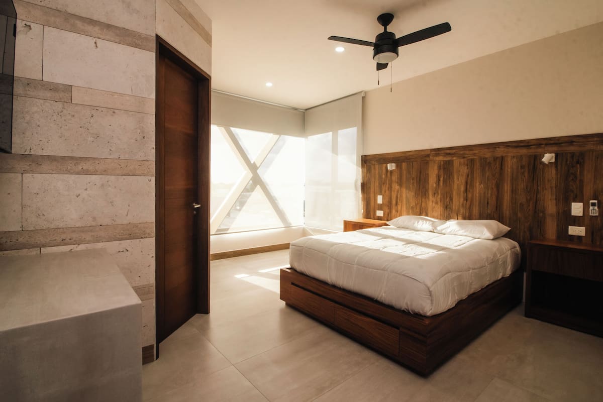 A modern bedroom with a wooden headboard, a large bed, a nightstand, and a ceiling fan.