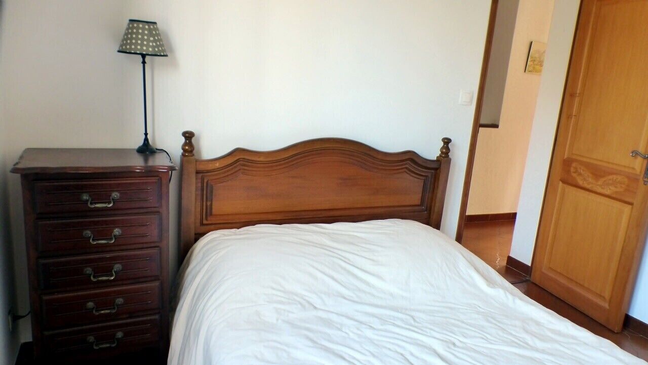 Un dormitorio con cabecera de madera, cómoda de madera con cajones y una lámpara.
