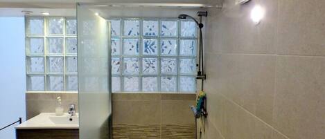 Une salle de bain avec une douche à parois de verre, un lavabo doté d’un distributeur de savon et un porte-serviettes.