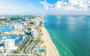 An aerial view of a coastal city with a marina, beachfront hotels, and a clear blue sea.