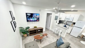 Un salon moderne avec un canapé gris, une table basse en bois et un téléviseur fixé au mur diffusant un film.
