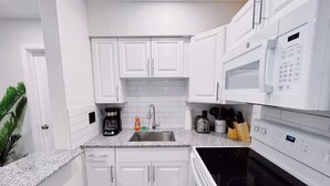 Une cuisine moderne avec des meubles blancs, un plan de travail en granit, un four à micro-ondes encastré et une cuisinière.