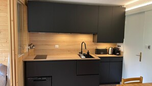 Une cuisine de taille réduite, avec des meubles de rangement sombres, un plan de travail en bois, un évier et un lave-vaisselle.