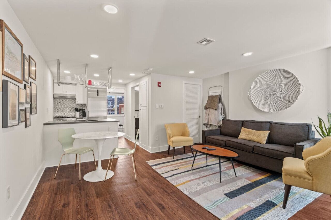 A modern living room with a sofa, armchairs, a coffee table, and a dining area with chairs and a table.