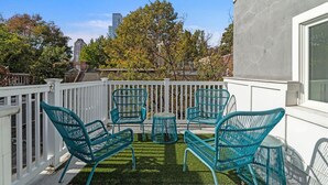 Ein Balkon mit vier türkisblauen Stühlen und einem kleinen runden Tisch, umgeben von einem weißen Geländer.