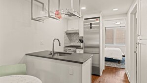 Eine kompakte Küche mit Spüle, Herd und Kühlschrank, ein kleiner Essbereich mit Tisch und ein Schlafzimmer mit Bett und Fenster.