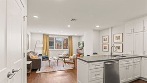 A modern kitchen with white cabinetry, a built-in dishwasher, and a dining area with a table and chairs. - Washington Square Gem | Patio! (Philadelphia)