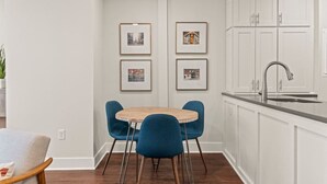 A kitchen with white cabinets, a round wooden table, and blue chairs. There are framed pictures on the wall. - Washington Square Gem | Patio! (Philadelphia)