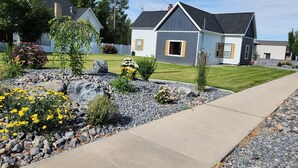 A residential house with a well-maintained lawn, a stone pathway, and a variety of flowering plants.