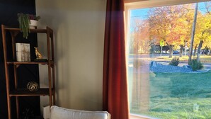 A cozy room with a wooden chair, a small table with a monkey figurine, a bookshelf, and a window with a view of trees.