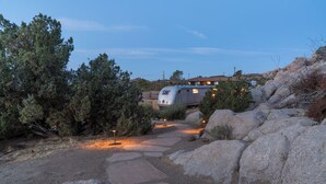 A campsite with a trailer, surrounded by rocks and trees, with a clear sky. - Desert Nest: Cozy Retreat Amidst Boulders (Yucca Valley)