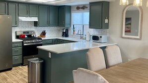 Eine moderne Küche mit grünen Schränken, einem Edelstahlkühlschrank, einer großen Kücheninsel und einem Essbereich mit Holztisch und Stühlen.
