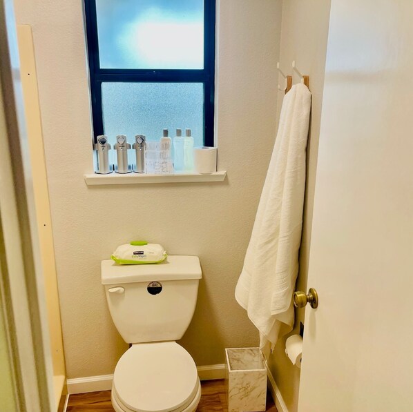 Uma casa de banho pequena com sanita, janela sobre a pia e uma toalha pendurada na porta.