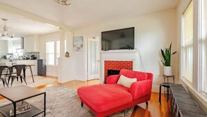 A modern living room with a red sofa, a fireplace, a flat-screen TV, and a dining area with a kitchen in the background.