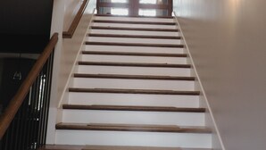 Una escalera de madera con barandilla que conduce a una puerta con paneles de vidrio.