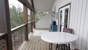 Una terraza de madera con una mesa redonda y sillas, un mueble azul pequeño y una puerta con un cartel.