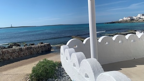 A coastal view with a white building, a stone wall, and a clear blue sky. - Charming spacious villa, 200 m from the sea, swimming pool, garden, AC, wifi... (Marina de Son Ganxo)
