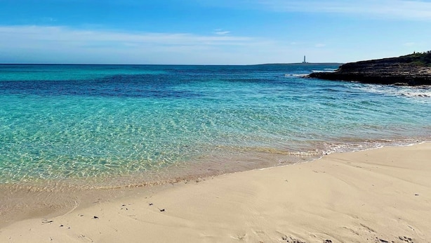 A beach with clear turquoise water, a sandy shore, and a lighthouse in the distance. - Charming spacious villa, 200 m from the sea, swimming pool, garden, AC, wifi... (Marina de Son Ganxo)