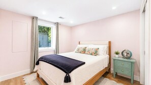 A bedroom with a bed, a nightstand, a window, and a view of greenery outside.