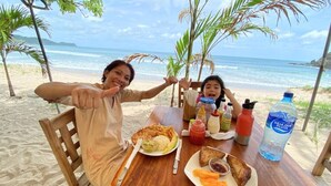 Ein Holztisch mit Mahlzeit, Gewürzen und einer Wasserflasche am Strand.