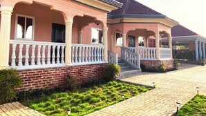 A two-story building with a pink facade, white columns, and a brick base. - Africa Waka Waka (Lungi)