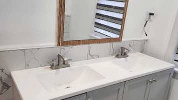 A bathroom with a double sink vanity, a large mirror with a wooden frame, and marble-patterned walls.