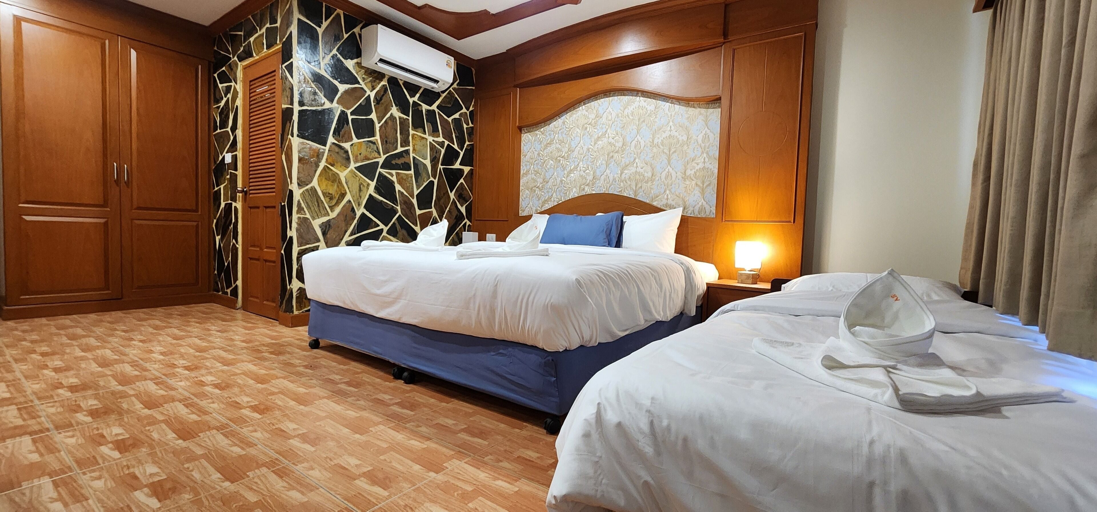 A hotel room with a large bed, a smaller bed, wooden cabinets, a stone wall, and a patterned headboard.