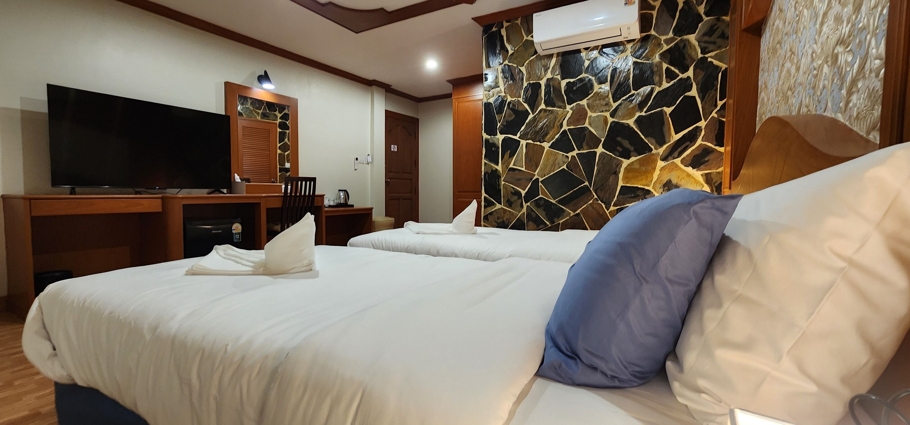 Habitación de hotel con dos camas, un televisor de pantalla plana, un escritorio y una pared de piedra.
