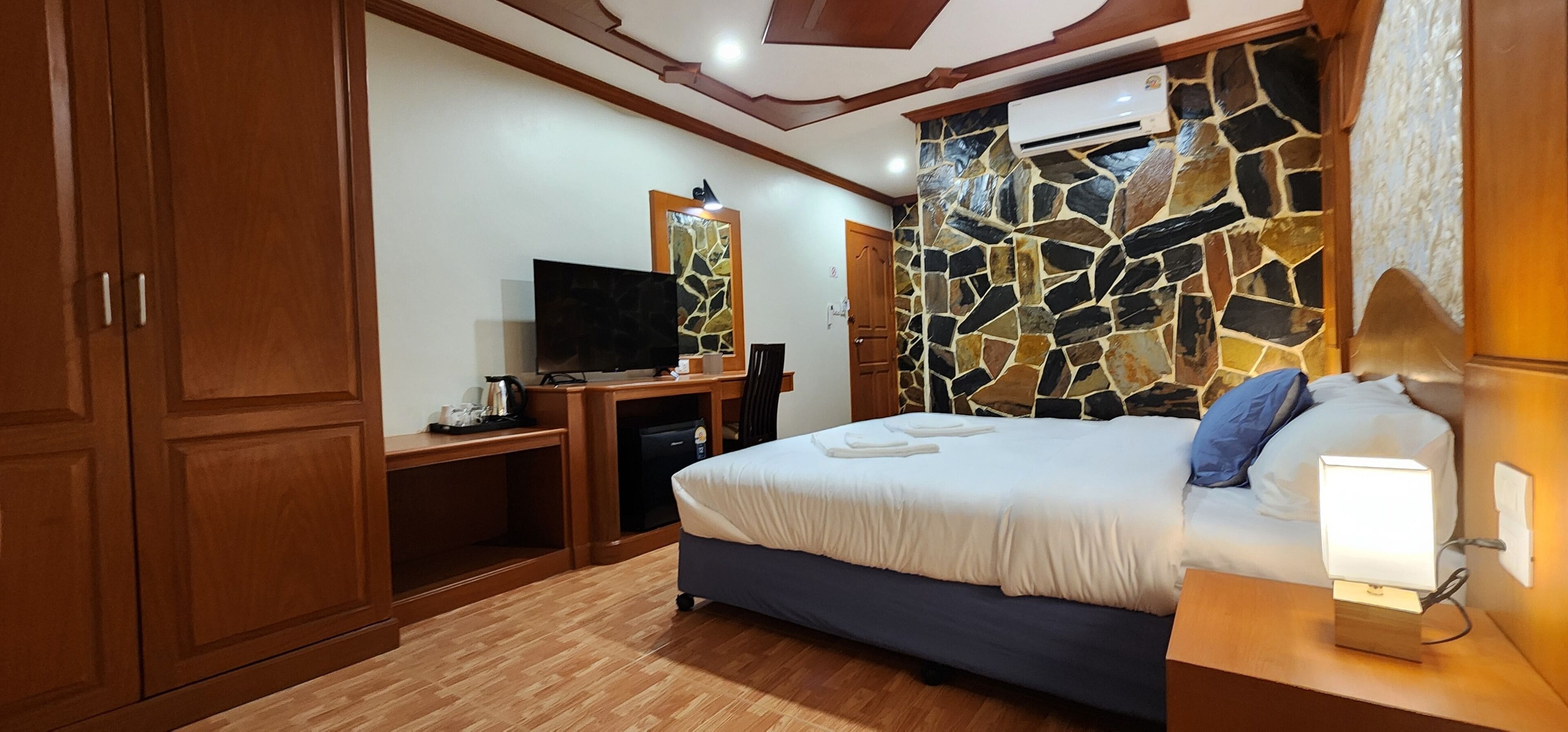 Un dormitorio con cama, televisión, escritorio y pared de piedra.