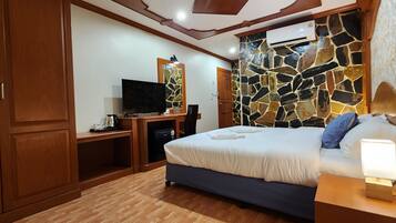 Un dormitorio con cama, televisión, escritorio y pared de piedra.